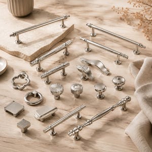 Op de afbeelding: Een collectie meubelbeslag van zilverkleurig metaal, bestaande uit diverse ladehandgrepen, knoppen en grepen. Het assortiment bevat gladde, getextureerde en gedessineerde afwerkingen in uiteenlopende vormen zoals rond, vierkant en langwerpig.