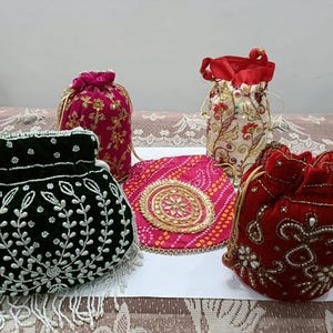 May include: A collection of four drawstring pouches featuring a dark green velvet bag with white beadwork, a magenta velvet bag with gold embroidery, a cream bag with floral patterns, and a red velvet bag with intricate gold and pearl beadwork.