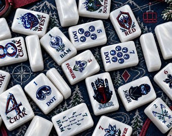 Könnte beinhalten: Eine Sammlung weißer Mahjong-Spielsteine mit farbenfrohen Illustrationen von Wintersportausrüstung, Berglandschaften und Blumenmotiven. Jeder Spielstein zeigt spezifische Textbeschriftungen wie West, Red, Dot, Bam, Crak, Flower und Joker in blauer oder roter Tinte.