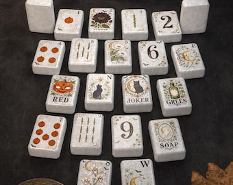 May include: A set of rectangular white tiles featuring various illustrations including pumpkins, flowers, cats, moons, and text such as RED, GREEN, SOAP, JOKER, and numbers. The tiles are arranged in a grid-like pattern on a dark surface.