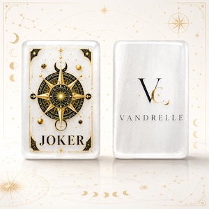 Puede incluir: Dos cartas de juego rectangulares blancas con esquinas redondeadas. La carta izquierda presenta un dise&ntilde;o de br&uacute;jula en oro y negro con la palabra JOKER. La carta derecha muestra un logotipo negro con las letras VC y el nombre VANDRELLE.