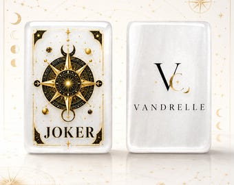 Puede incluir: Dos cartas de juego rectangulares blancas con esquinas redondeadas. La carta izquierda presenta un diseño de brújula en oro y negro con la palabra JOKER. La carta derecha muestra un logotipo negro con las letras VC y el nombre VANDRELLE.