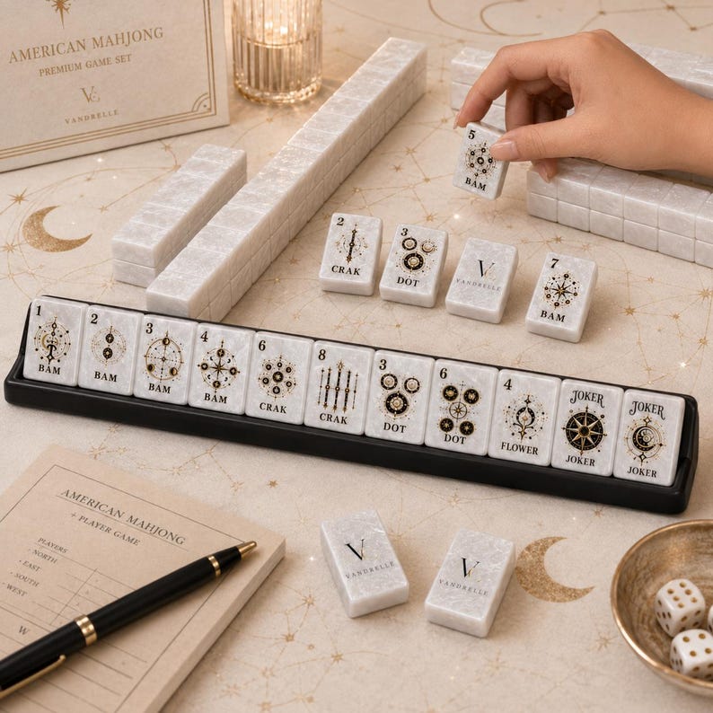 Puede incluir: Un juego de Mahjong americano con fichas de m&aacute;rmol blanco y grabados dorados de tem&aacute;tica celestial. El set incluye un soporte negro para fichas, una libreta de puntuaci&oacute;n, un bol&iacute;grafo, dados y una caja con el texto American Mahjong Premium Game Set.