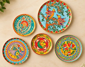 May include: A set of five round decorative plates featuring vibrant, multi-colored hand-painted designs. The patterns include stylized birds on branches, floral motifs, and geometric borders in shades of red, yellow, blue, and green.