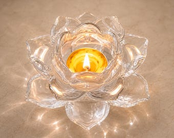 Puede incluir: Un portavelas de cristal transparente con forma de flor de loto en flor con pétalos superpuestos. Una pequeña copa redonda de metal para velas de té se encuentra en el centro, conteniendo una vela encendida con una llama amarilla brillante.