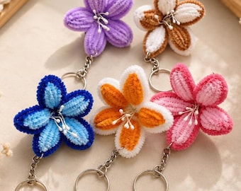May include: Five fuzzy flower keychains in purple, brown and white, blue, orange and white, and pink. Each flower features five petals made of pipe cleaner material with white stamens in the center, attached to a silver metal chain and ring.