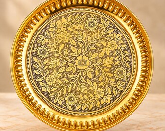 May include: A round gold-colored metal tray featuring an intricate embossed floral pattern across the center. The surface displays a detailed design of flowers and leaves against a dark, textured background, framed by a scalloped edge.