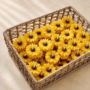 Pode incluir: Uma cesta retangular de vime trançado cheia de inúmeras pequenas velas em formato de girassol. Cada vela apresenta pétalas amarelo-brilhantes e um centro texturizado marrom-escuro com um pavio branco saindo do meio, dispostas em um grupo.