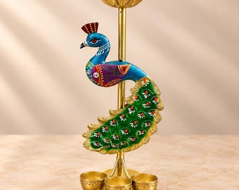 Puede incluir: Un candelabro de metal dorado con una varilla vertical central rematada por un cuenco festoneado. Una figura decorativa de pavo real con detalles pintados en azul, verde y morado está unida a la varilla, sobre tres pequeños soportes circulares.