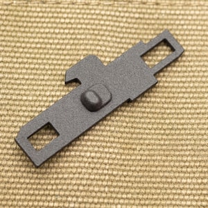 May include: A matte black metal component featuring a flat, elongated rectangular body with a central raised protrusion, a small notch on one side, and square-shaped cutouts at both ends, designed for mechanical assembly or hardware applications.
