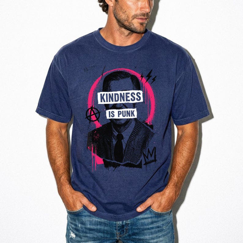 Pode incluir: Uma t-shirt azul-marinho de manga curta com uma estampa gr&aacute;fica de uma pessoa de fato e gravata. O design inclui um c&iacute;rculo rosa brilhante, um s&iacute;mbolo de anarquia e o texto branco "KINDNESS IS PUNK" sobre o centro do rosto.