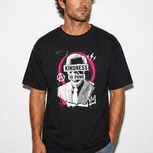 Pode incluir: Uma t-shirt preta com uma estampa gr&aacute;fica de uma pessoa com camisa de colarinho e gravata. O design inclui um fundo circular rosa, um s&iacute;mbolo de anarquia e o texto "KINDNESS IS PUNK" em branco sobre a &aacute;rea dos olhos e da boca.