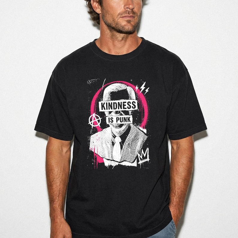 Pode incluir: Uma t-shirt preta com uma estampa gr&aacute;fica de uma pessoa com camisa de colarinho e gravata. O design inclui um fundo circular rosa, um s&iacute;mbolo de anarquia e o texto "KINDNESS IS PUNK" em branco sobre a &aacute;rea dos olhos e da boca.