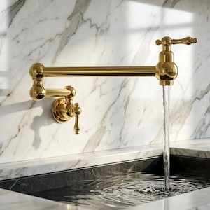 May include: A wall-mounted, articulated pot filler faucet with a polished gold finish. The faucet features two joints for extending the arm and a single lever handle. Water flows from the spout into a sink, demonstrating the functional design.