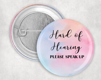 Puede incluir: Un botón de acuarela rosa y azul con el texto "Hard of Hearing Please Speak Up".