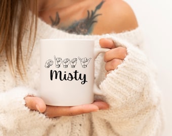 Pode incluir: Caneca de cerâmica branca com um design preto. O design inclui o nome "Misty" e as letras do nome escritas em linguagem de sinais americana.