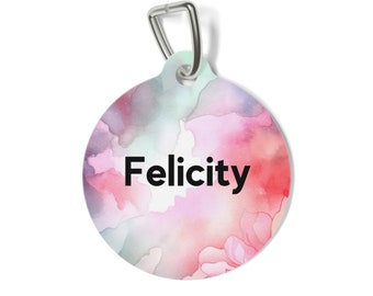 Puede incluir: Una placa de identificación circular para mascotas con un fondo estilo acuarela en tonos mezclados de rosa, morado y azul claro. El nombre Felicity está impreso en letras negras negritas en el centro. Incluye una anilla de metal plateado.