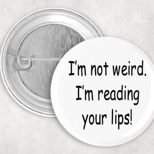 Puede incluir: Un botón blanco con el texto "I'm not weird. I'm reading your lips!" en negro. El botón tiene una parte trasera de metal plateado con un cierre de imperdible.