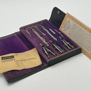 May include: A vintage Dietzgen drafting instrument set in a black case with a purple velvet interior. The set includes various metal compasses and dividers. A small beige cloth with the text Dietzgen and a paper policy document are included.