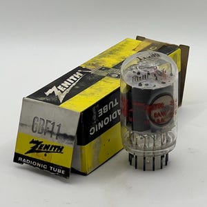 May include: A clear glass Zenith 6BF11 Radionic vacuum tube with internal metal components and pins at the base. It is positioned next to its original yellow and black cardboard box, which features the Zenith logo and the text 6BF11 Radionic Tube.