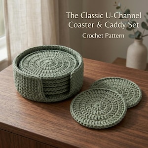 Op de afbeelding: Een saliegroene gehaakte onderzetterset bestaande uit een ronde houder met een U-vormige uitsparing en diverse bijpassende ronde onderzetters. De tekst The Classic U-Channel Coaster & Caddy Set Crochet Pattern is zichtbaar in de afbeelding.