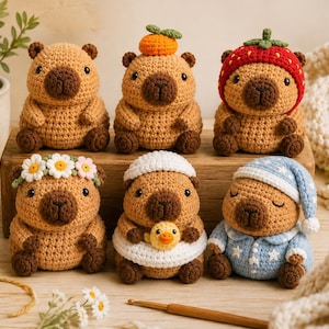 Könnte beinhalten: Sechs kleine, hellbraune, gehäkelte Capybara-Figuren in zwei Reihen. Die obere Reihe zeigt ein schlichtes Capybara, eines mit einem orangefarbenen Hut und eines mit einem Erdbeerhut. Die untere Reihe umfasst eines mit Gänseblümchenkranz, eines mit Entenschwimmring und eines im Schlafanzug.