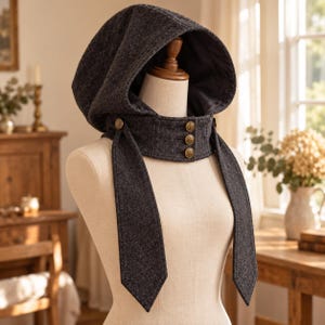 May include: A dark gray wool-blend hood with a structured collar featuring three decorative brass-toned buttons. The hood has long, pointed side panels that drape downward, and the collar is secured with matching brass-toned buttons.