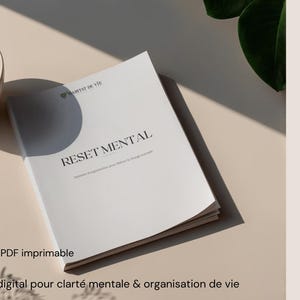 Pode incluir: Um documento branco intitulado RESET MENTAL com o texto 56 pages PDF imprimable e Planner digital pour clarté mentale & organisation de vie, acompanhado por uma chávena de cerâmica bege cheia de café líquido escuro.
