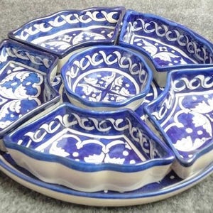 Puede incluir: Una bandeja de servicio circular de cerámica con un cuenco central redondo rodeado por cuatro platos en forma de abanico. El conjunto está decorado con un patrón floral pintado a mano en azul y blanco y bordes festoneados. El texto 2.6 KG es visible.