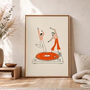 Peut inclure: Une affiche encadrée représentant un dessin au trait de deux personnages dansant sur un grand disque vinyle orange posé sur une platine. Les personnages portent des hauts à motifs orange et des pantalons orange sur un fond crème clair.