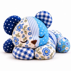 May include: A stuffed bear toy crafted from various blue and white fabric patterns, including floral prints, gingham checks, and polka dots. The bear is in a sleeping position with closed eyes, a brown nose, and rounded ears, featuring a patchwork design.