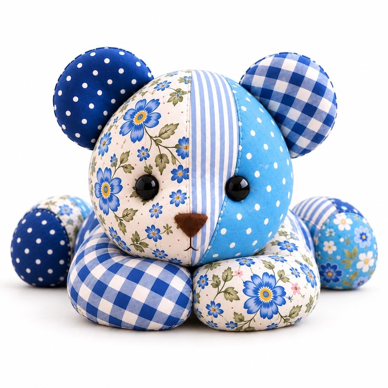 May include: A stuffed bear toy constructed from various blue and white fabric patches. The head features floral, striped, and polka-dot patterns with black button eyes and a brown nose. The ears and limbs display gingham, polka-dot, and floral prints.