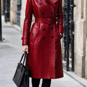 Peut inclure: Un trench-coat rouge brillant avec une texture gaufrée façon crocodile, doté d'une fermeture à double boutonnage avec des boutons noirs, d'une ceinture assortie, de pattes d'épaule et d'un large col. Porté sur un col roulé et un pantalon noirs.