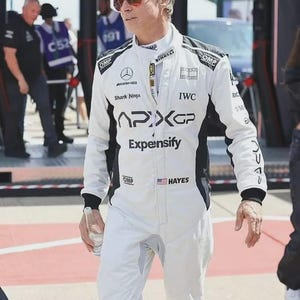 Puede incluir: Un traje de carreras blanco y negro con el texto APXGP, Expensify, Shark Ninja, IWC y OMP. El traje incluye una pequeña bandera estadounidense junto al nombre HAYES, un logotipo de Mercedes-AMG y un logotipo de Pirelli en el pecho.