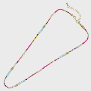 Puede incluir: Un collar de cuentas con una vibrante variedad de pequeñas cuentas multicolores, intercaladas con cuentas cúbicas de color azul claro más grandes y espaciadores cilíndricos dorados. El collar incluye una cadena extensora dorada y un cierre de mosquetón.