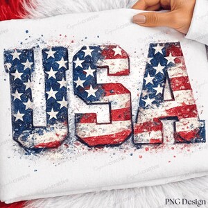 Peut inclure: Un vêtement en tissu blanc arborant les lettres USA dans une police grasse et imposante. Les lettres sont remplies d'un motif de drapeau américain vieilli en rouge, blanc et bleu, avec un effet d'éclaboussures de peinture aquarelle.