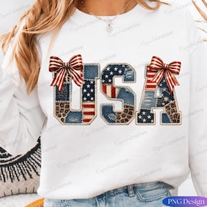Puede incluir: Una sudadera blanca de manga larga con las letras USA en un diseño de patchwork. Las letras están compuestas por texturas de mezclilla, patrones de bandera estadounidense y estampado de leopardo, con dos lazos a rayas rojas y blancas.