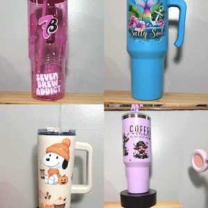 May include: Four tall tumblers with lids and straws. One is translucent pink with 'Seven Brew Addict' text. One is light blue with a mermaid tail and 'Salty Soul' text. One is cream with a Snoopy graphic. One is light purple with 'Coffee Mode' text.
