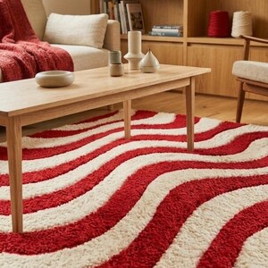 May include: A rectangular area rug featuring a high-pile texture with alternating wavy stripes in vibrant red and off-white. The rug covers the floor space beneath a light-toned wooden coffee table, showcasing a bold, flowing pattern throughout.