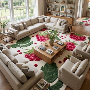 May include: A large area rug featuring a cream background with a repeating pattern of vibrant pink raspberries and large green leaves. The rug is positioned in a living room setting beneath a wooden coffee table, beige sofas, and armchairs.
