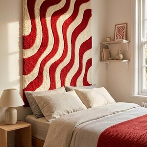 May include: A large rectangular wall hanging featuring a tufted texture with a repeating pattern of vertical wavy lines in alternating shades of deep red and cream. The textile piece is mounted on the wall above a bed with neutral bedding.