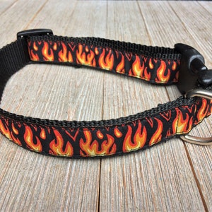 May include: Black dog collar with a red and yellow flame pattern. The collar has a black plastic buckle and a silver metal D-ring.