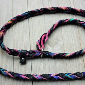 May include: A black leather dog leash with a braided design featuring pink, blue, and green accents. The leash has a metal ring and a leather loop at the end.