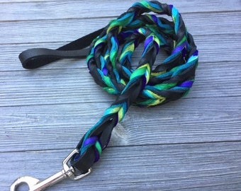 May include: A black leather dog lead with a braided design featuring green, blue and purple accents. The lead has a silver clip.