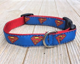 May include: A blue and red dog collar with a repeating pattern of the Superman logo. The collar has a black plastic buckle and a silver metal D-ring.