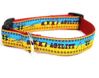 May include: Red, yellow, and blue dog collar with the word "Agility" printed on it. The collar has a black buckle and a silver D-ring.