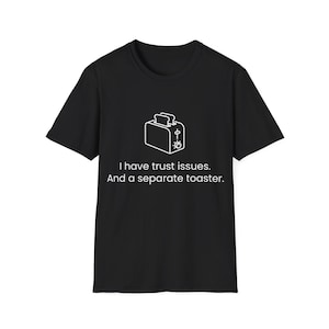 Puede incluir: Una camiseta negra de manga corta con un gráfico de líneas blancas de una tostadora centrado en el pecho. Debajo de la tostadora, el texto dice: I have trust issues. And a separate toaster. El diseño está impreso en una fuente blanca.