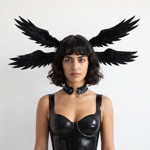 May include: A black headpiece featuring two pairs of feathered wings extending outward from the sides. The accessory is paired with a black ruffled choker featuring a central metal ring and a black sleeveless top with a glossy finish.
