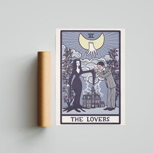 May include: A rectangular print featuring a tarot card design titled THE LOVERS, depicting a woman in a long black dress and a man in a striped suit standing before a house. Above them is a crescent moon with a hand, surrounded by rose bushes.