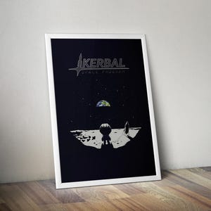May include: A framed vertical poster featuring a dark space scene with the text Kerbal Space Program at the top. A small astronaut figure stands on a cratered lunar surface looking toward a distant Earth, with a rocket ship nearby in the starry sky.